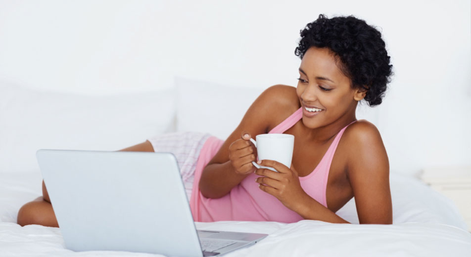 woman holding a coffee cup and using her laptop on a mattress