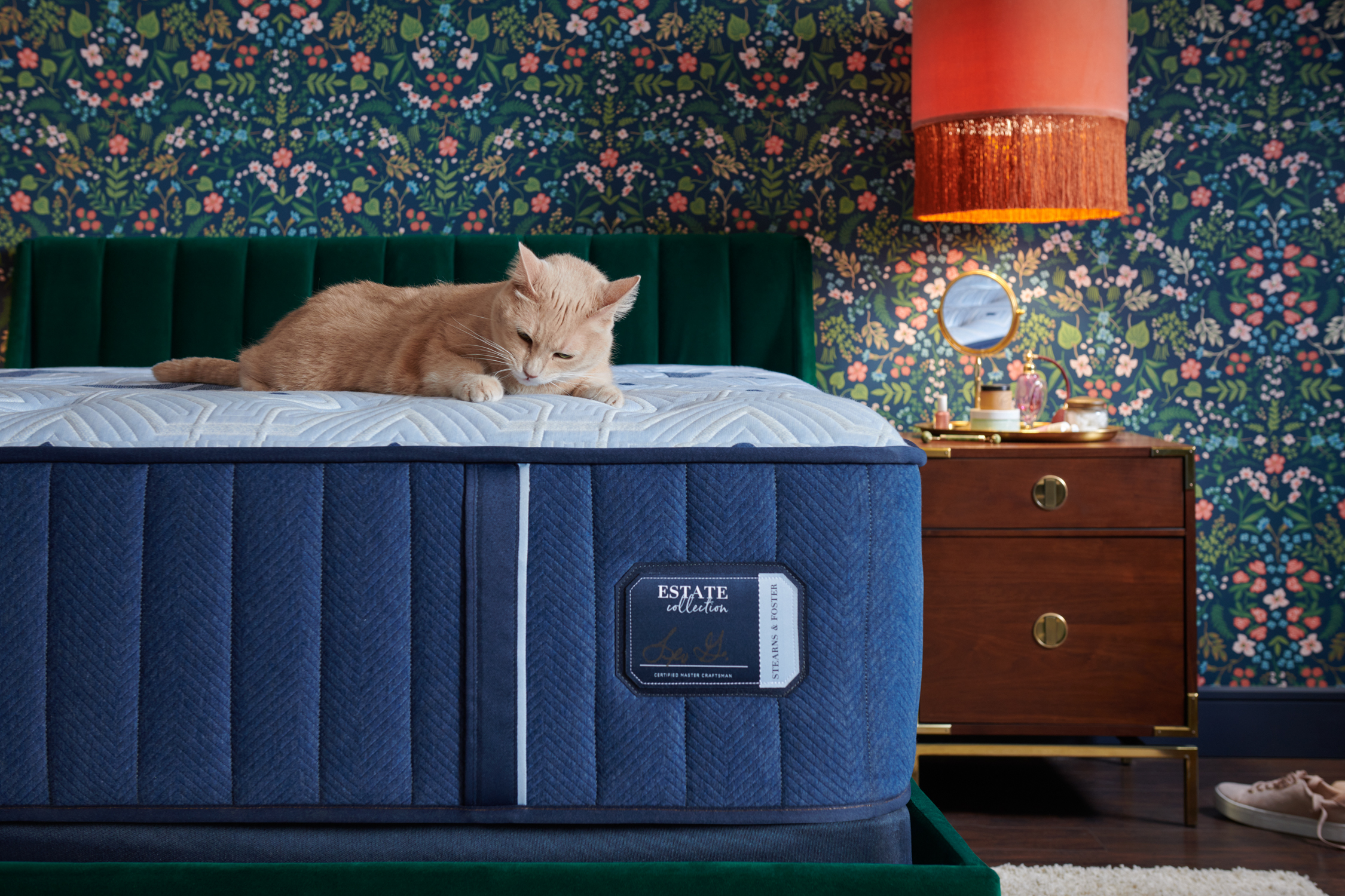orange cat napping on Stearns & Foster Reserves Estate mattress placed on a velvet green bed frame that is against a dark floral accent wall
